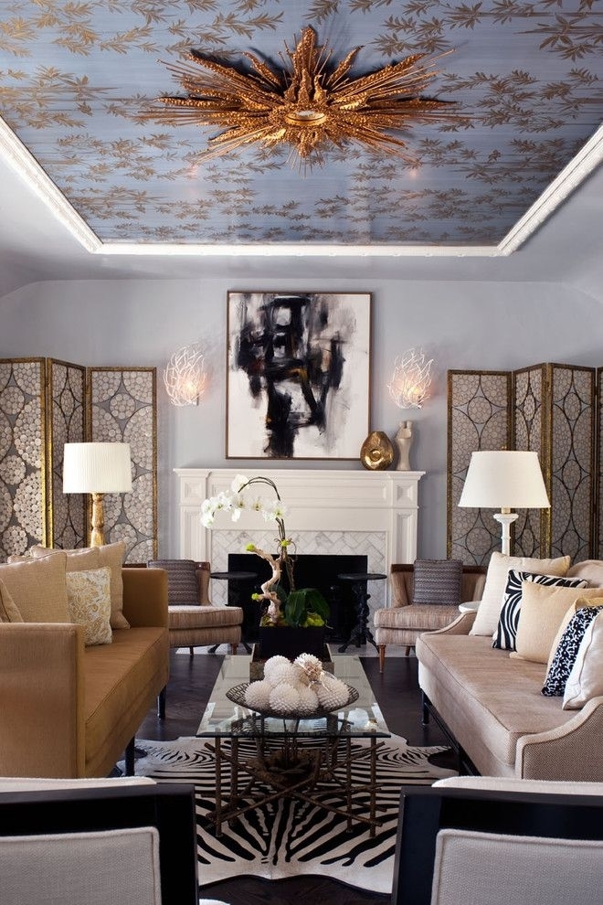 Золотистая люстра поддержана растительным рисунком того же цвета на натяжном потолке и золотистым декором самой гостиной